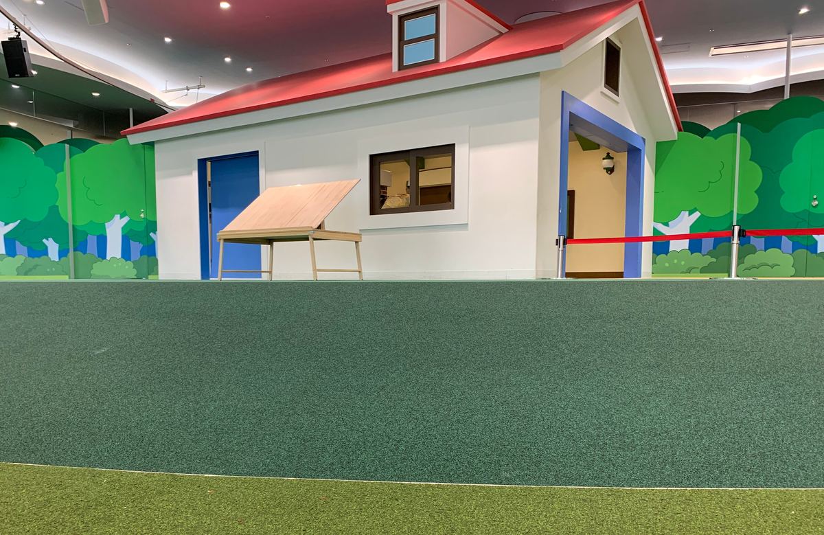 A house-shaped play structure on soft green turf inside the museum