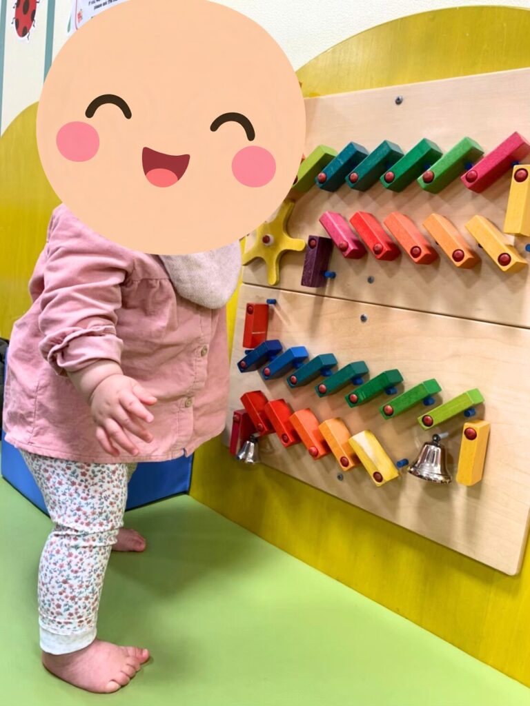 A toddler using a colourful wall-mounted activity board in the baby play area