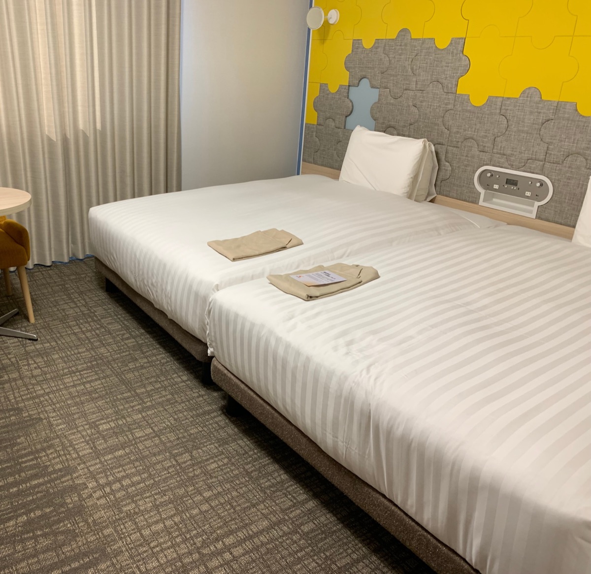 Hotel room with two beds and a colorful puzzle-piece wall panel behind the headboard