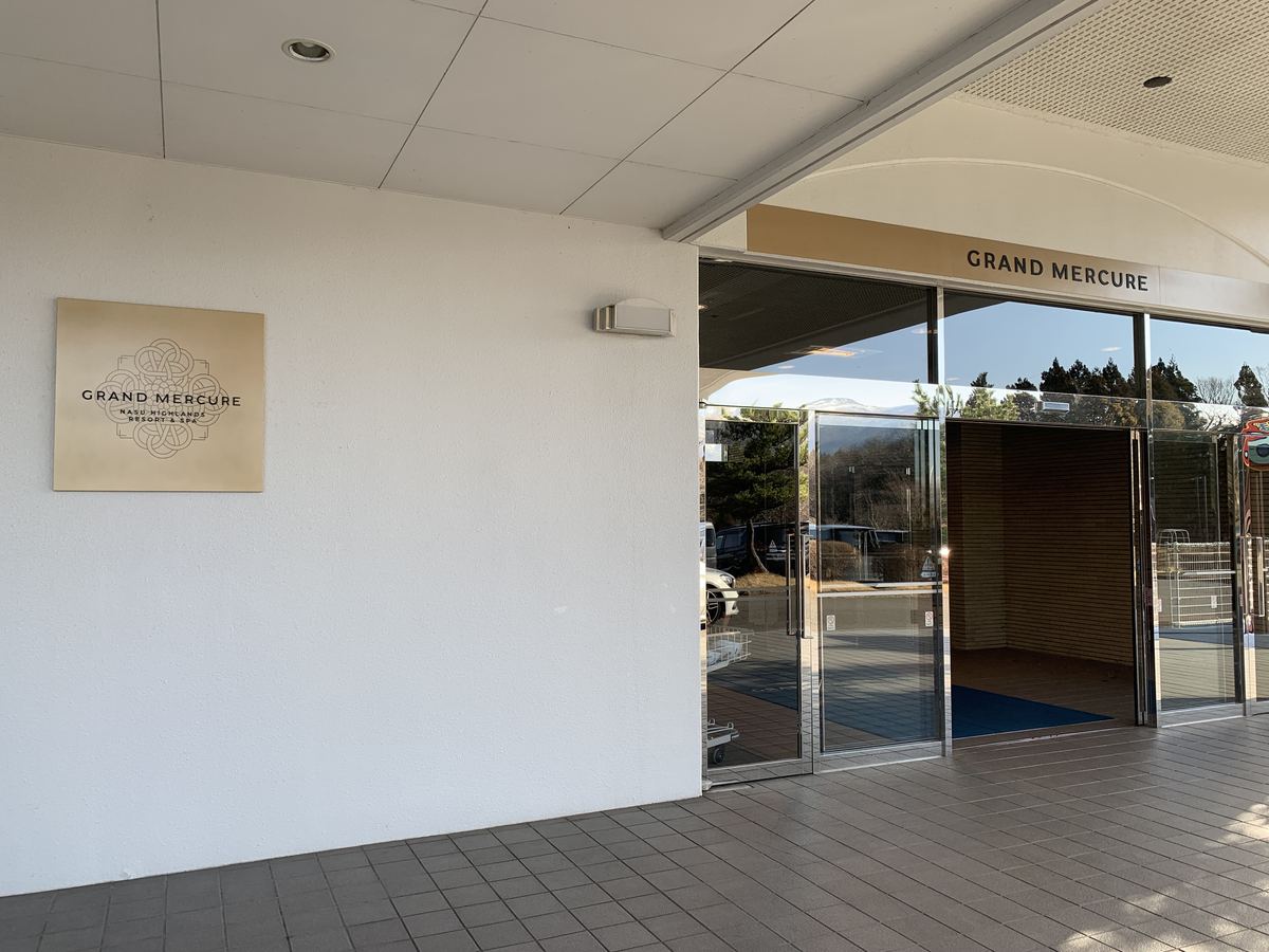 The entrance to Grand Mercure Nasu Highlands Resort & Spa, with the brass hotel sign and glass doors