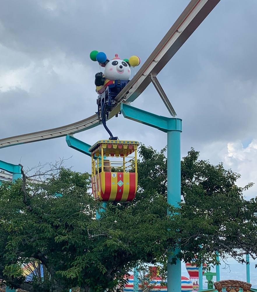 A kiddie monorail car topped with a panda balloon, running on its elevated track