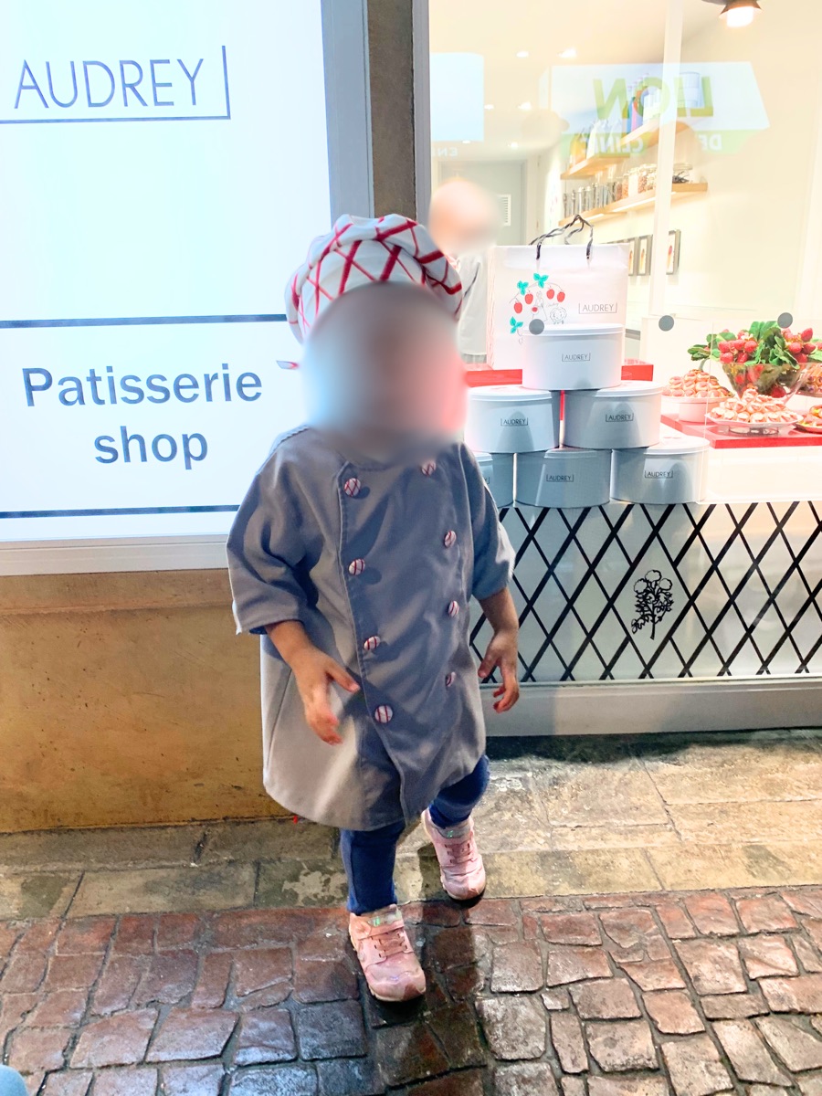 A child dressed in a pastry chef uniform outside the Patisserie shop
