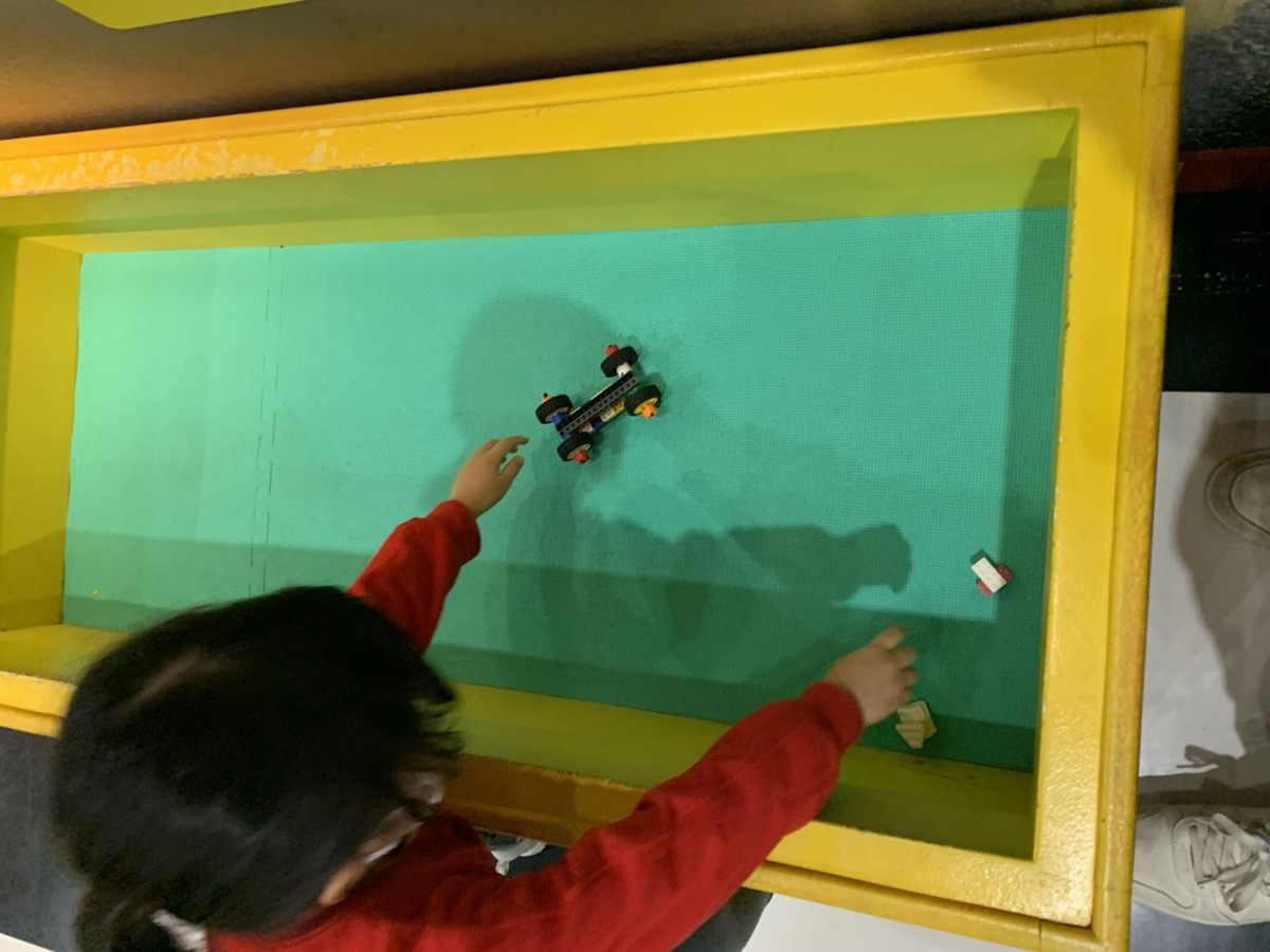 A child rolling a homemade LEGO race car down the speed track at the Racer Build & Test station