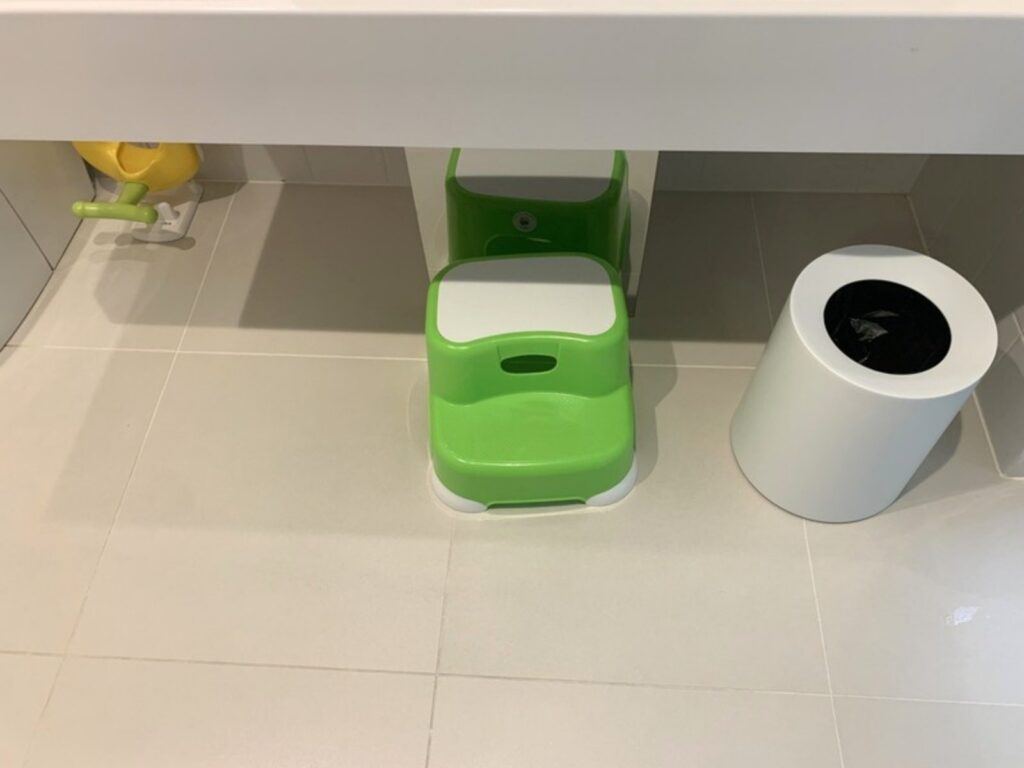 A green step stool and a lidded diaper bin in the room's restroom