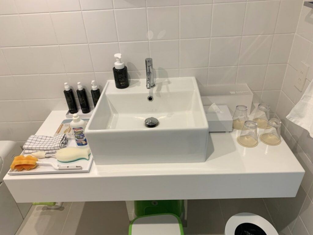 Bottle detergent and a brush on the washbasin counter, with a child's step stool below