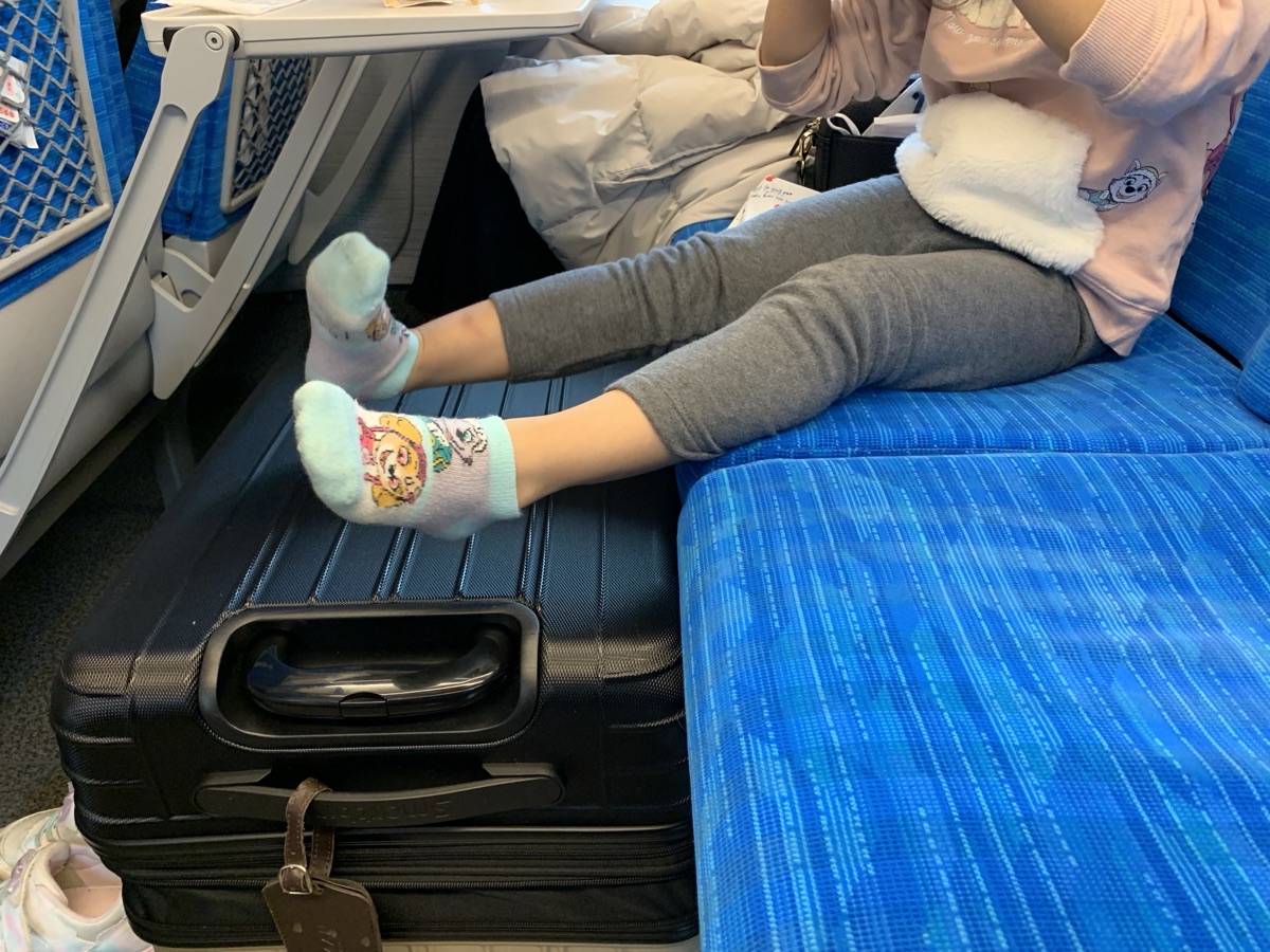 Child's feet resting on a suitcase in the oversized-luggage seat area of the Shinkansen