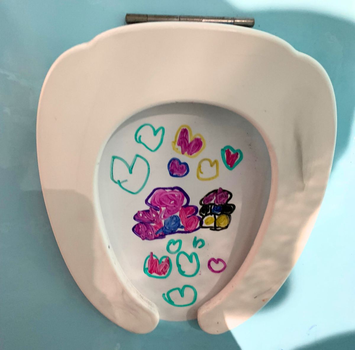 A toilet-seat-shaped canvas decorated with a child's colorful heart drawings